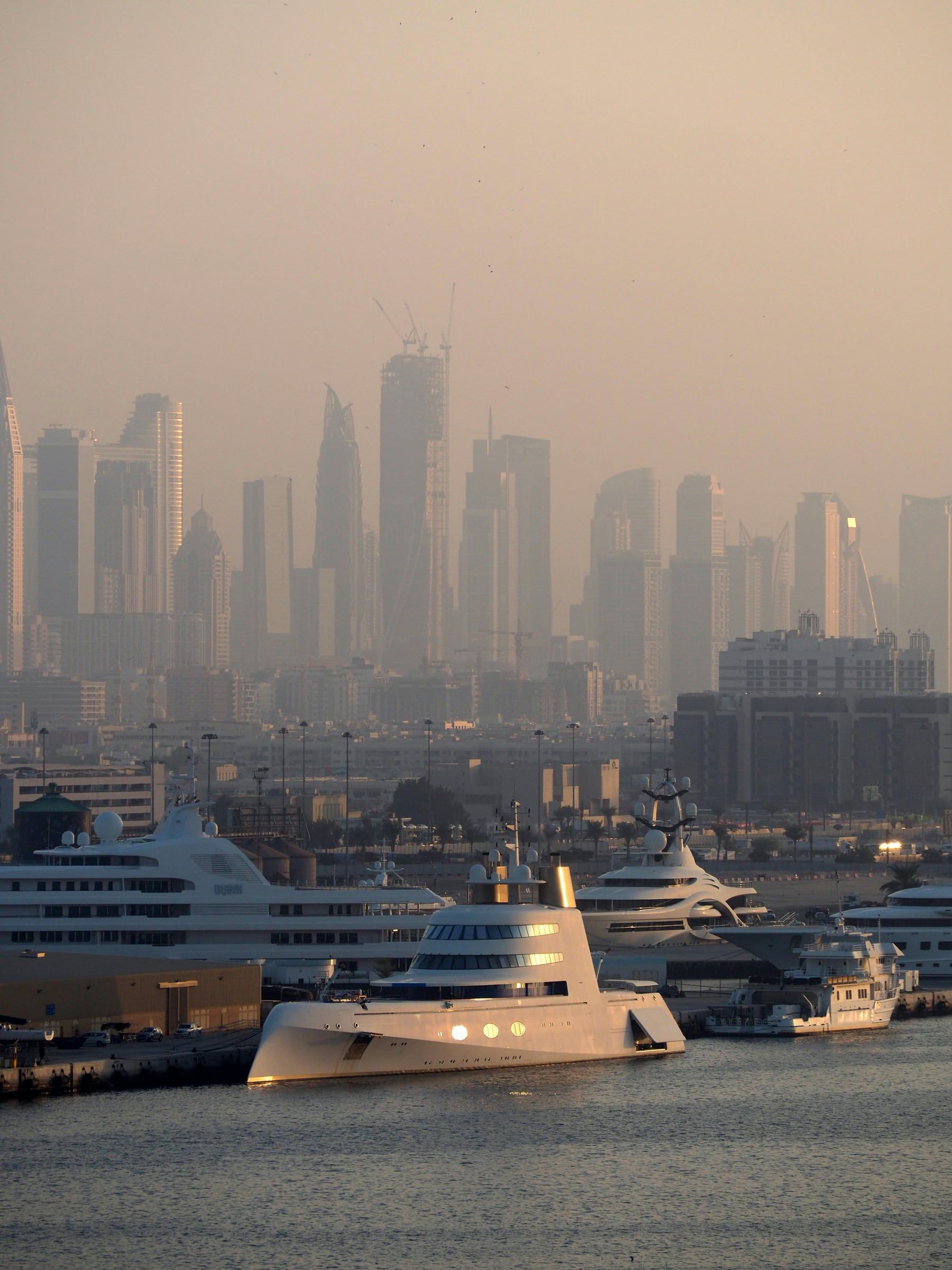 Dubai skyline in the evening haze, with yachts moored in the marina.